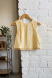 Yellow striped top on a hanger against a white brick wall.