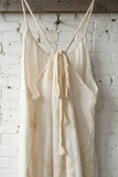 White embroidered dress hanging on a wooden rod against a white brick wall.