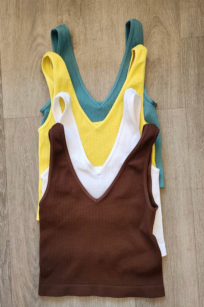 Three tank tops in yellow, brown, and green on a wooden surface