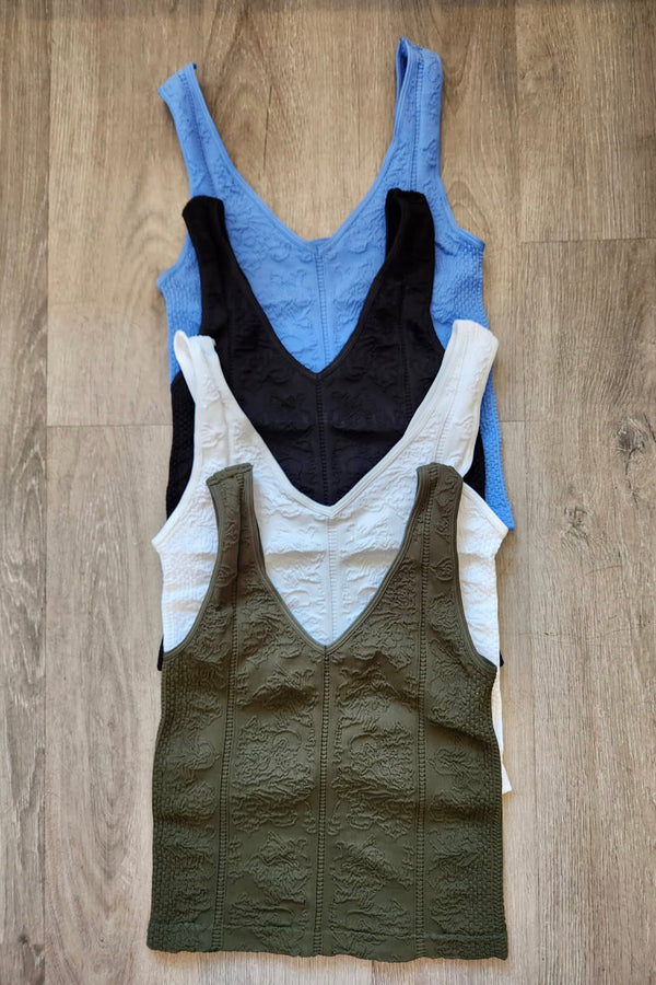 Four tank tops in blue, black, white, and green on a wooden surface