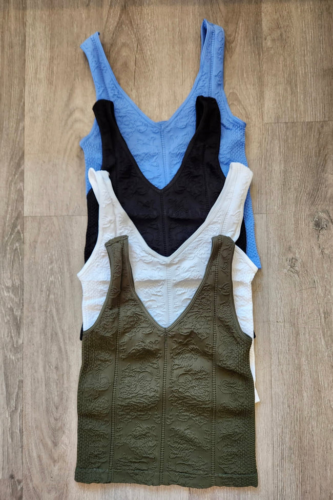 Four tank tops in blue, black, white, and green on a wooden surface