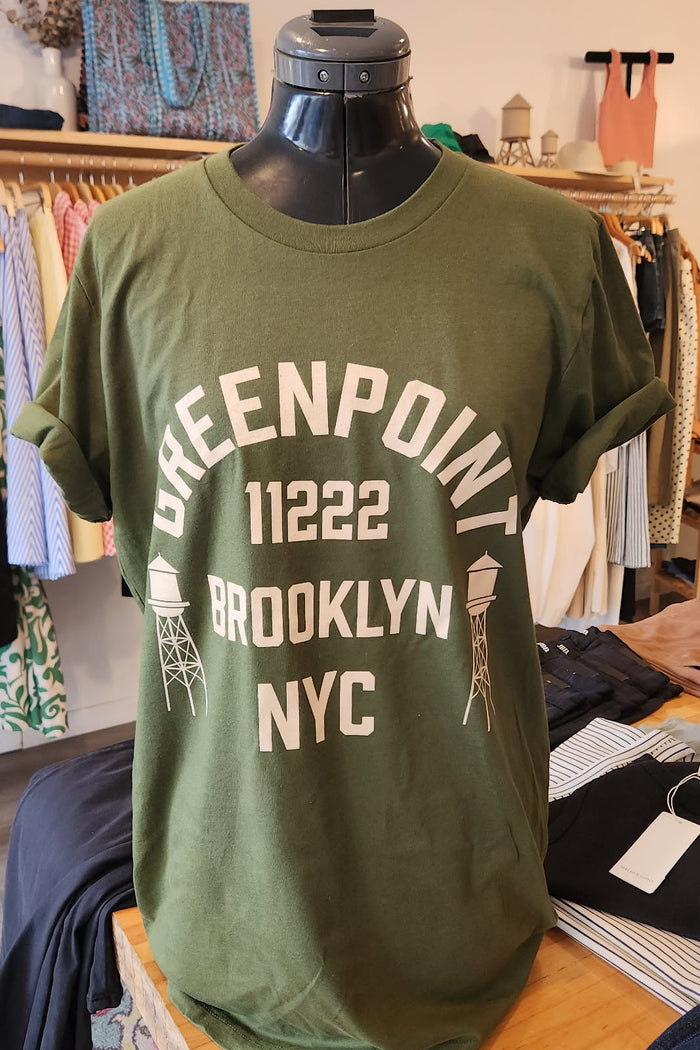 Green t-shirt with 'Greenpoint 11222 Brooklyn NYC' text on a mannequin in a store setting.