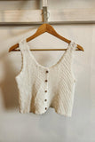 Knitted vest with buttons on a wooden hanger against a plain wall.