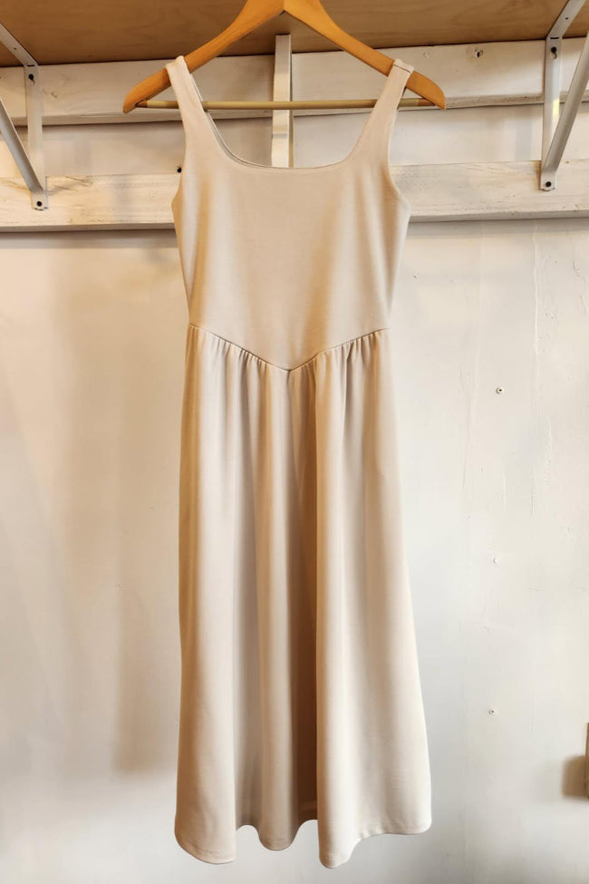 Beige dress hanging on a wooden hanger against a white wall.