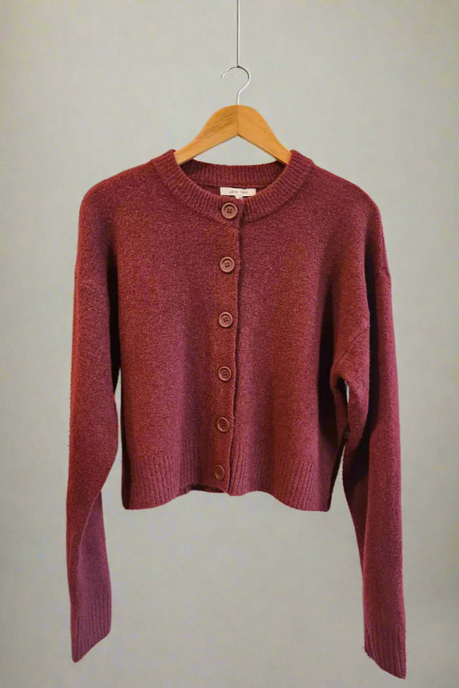 Maroon cardigan on a hanger against a plain background