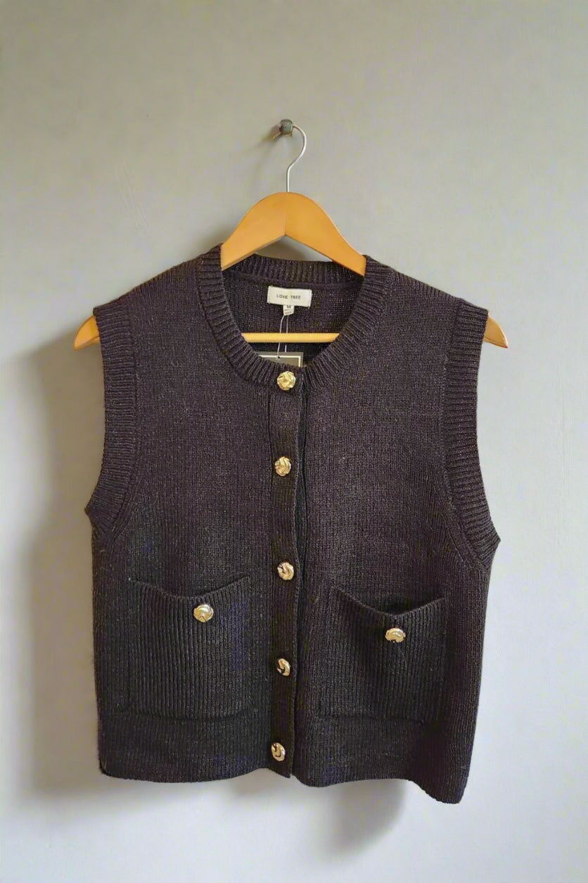 Black knitted vest with gold buttons on a wooden hanger against a neutral background