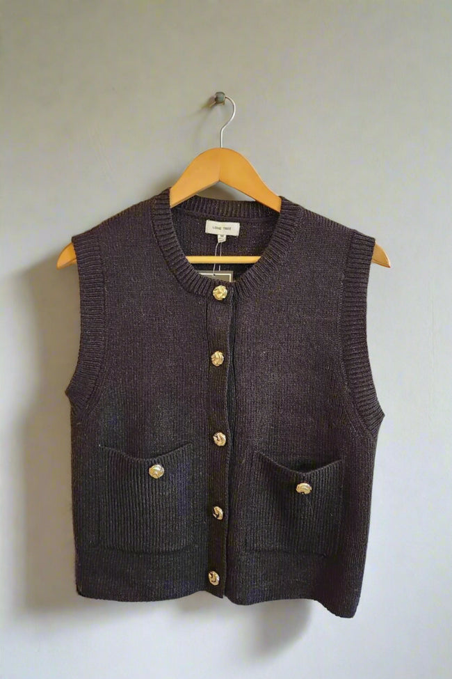 Black knitted vest with gold buttons on a wooden hanger against a neutral background