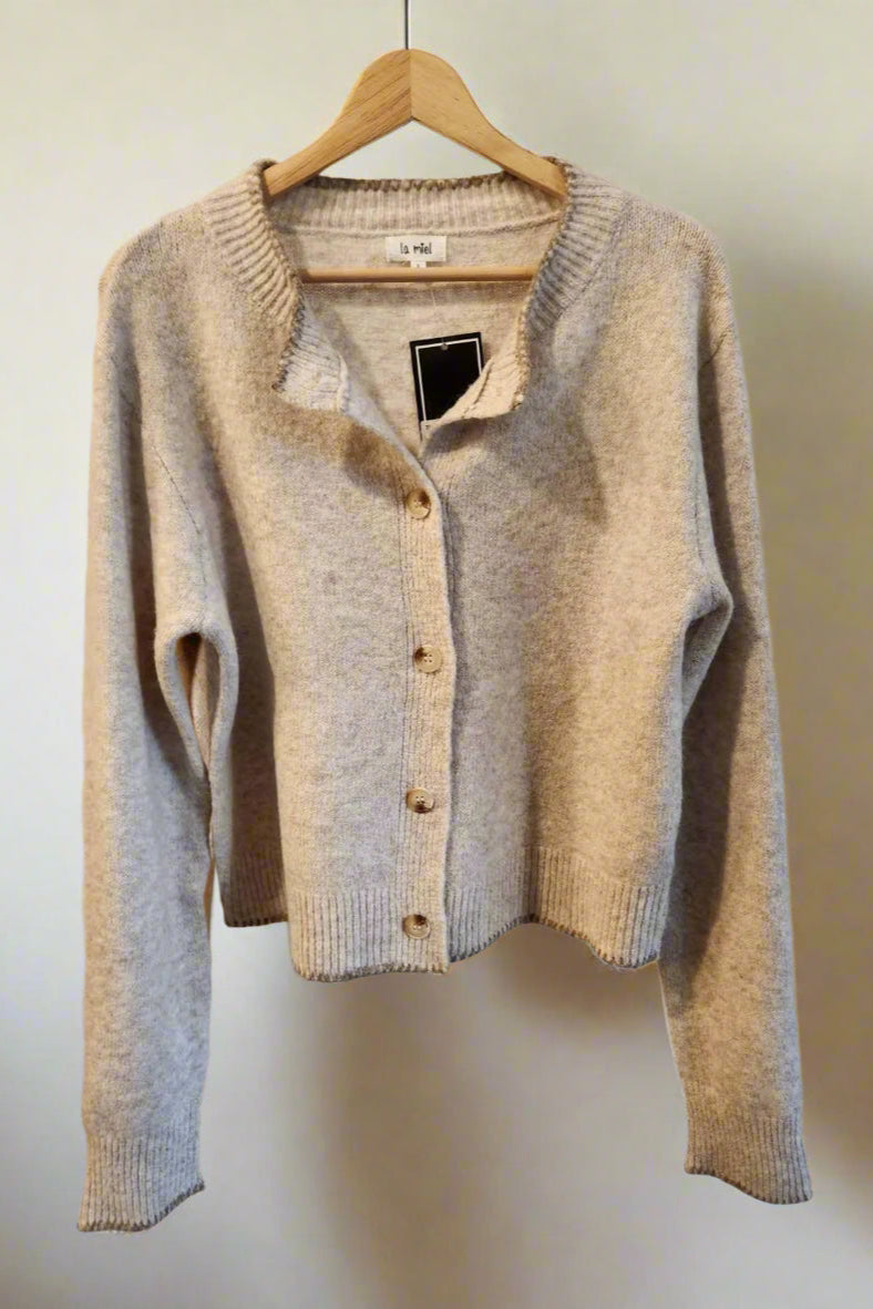 Beige cardigan on a hanger against a plain background
