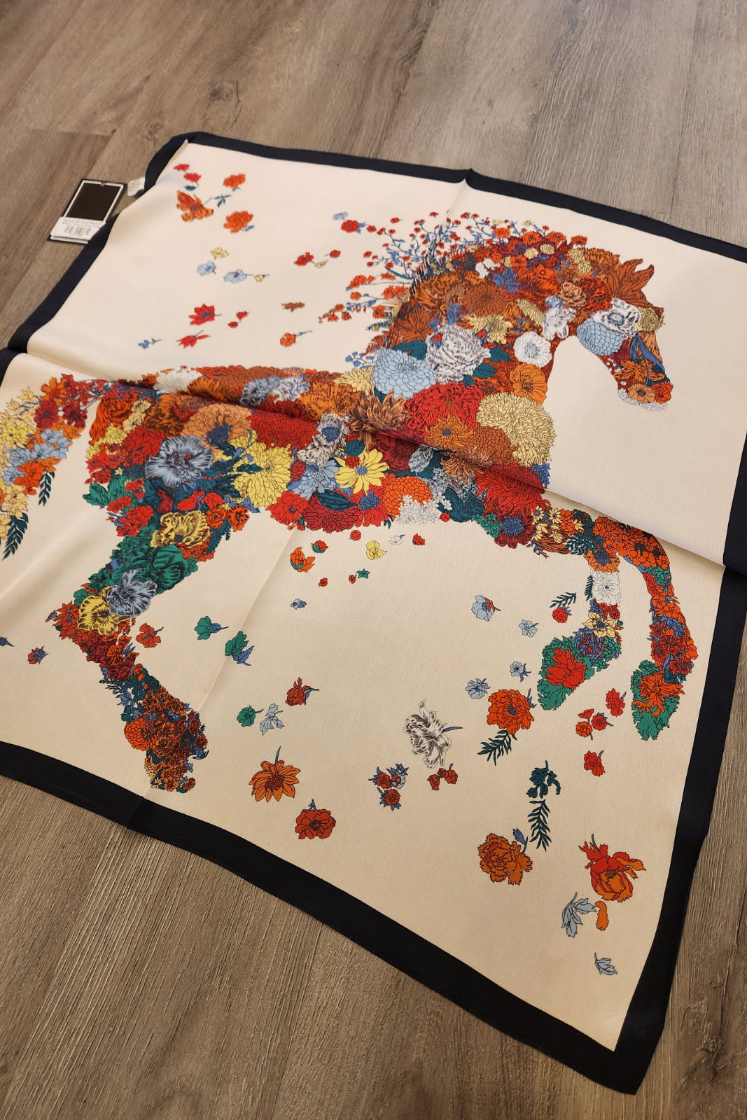 Floral-patterned horse design on a blanket laid on a wooden floor.