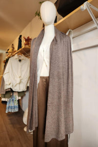 A mannequin dressed in a taupe knit open-front cardigan over a white top and brown pants, displayed inside a clothing boutique with racks and shelves visible in the background.