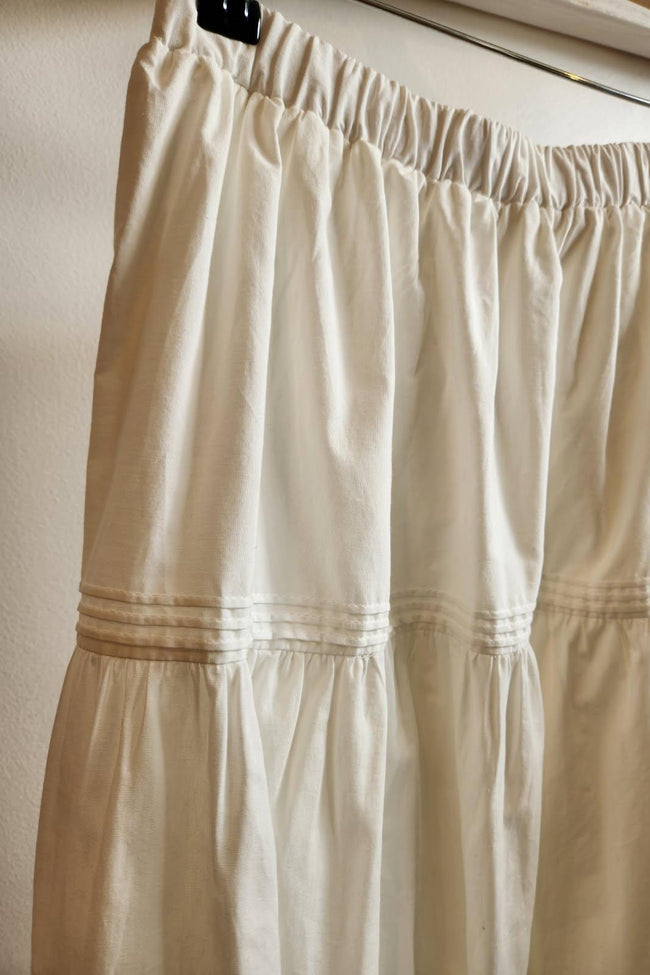 white skirt with a wooden hanger and clips on a neutral background