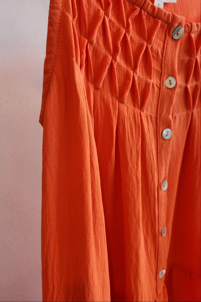 Close-up of orange dress with button details on a plain background