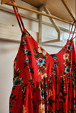 Red floral dress hanging on a wooden hanger against a neutral wall.