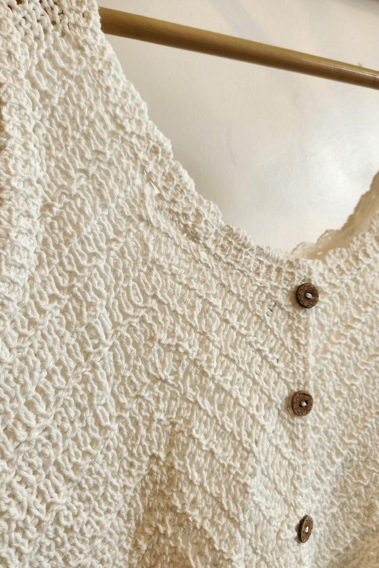 Close-up of a textured beige cardigan with buttons on a hanger.
