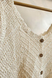 Close-up of a textured beige cardigan with buttons on a hanger.