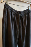 black drawstring pants hanging from a wooden hanger with metal clips against a plain wall.