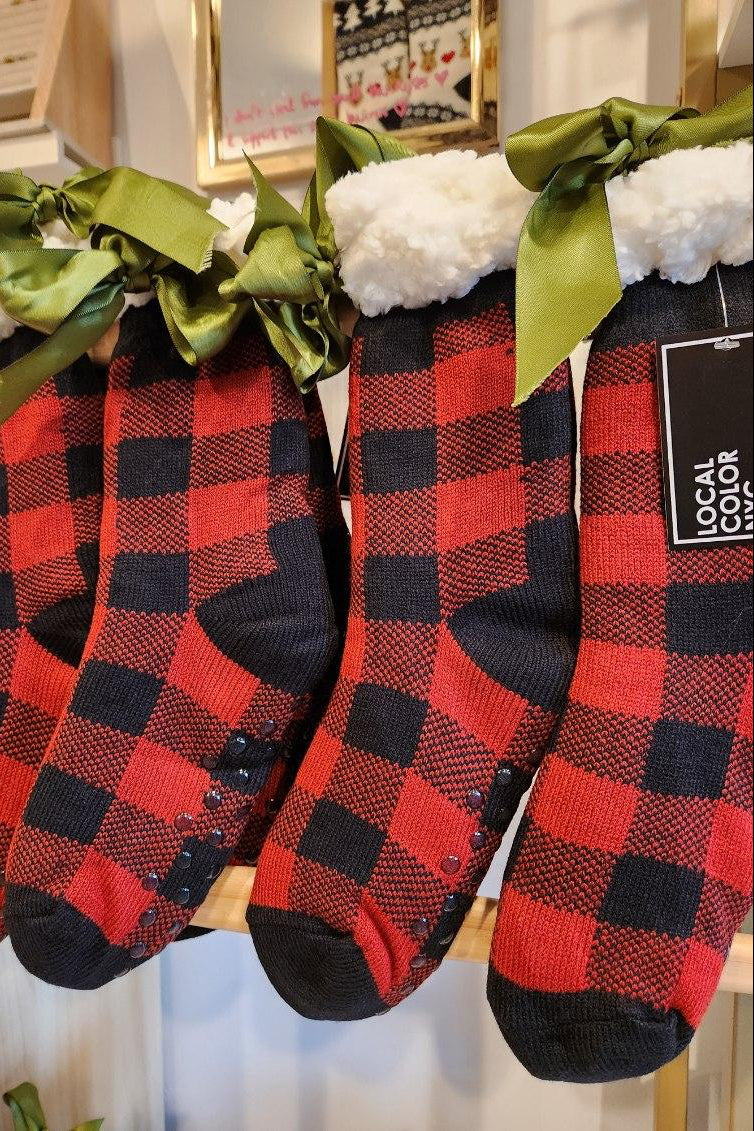 Red and black checkered socks with green bows on a wooden surface.