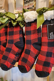 Red and black checkered socks with green bows on a wooden surface.