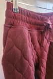 Maroon quilted pants hanging on a rack against a neutral background