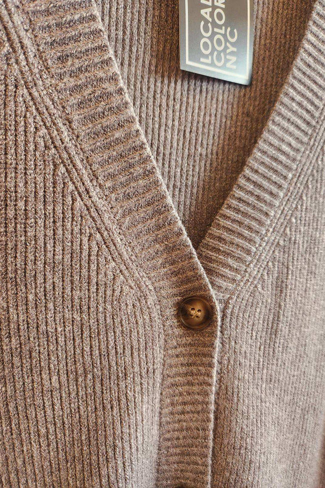 Close-up of a grey cardigan with a button and 'LOCAL COLOR NYC' label.