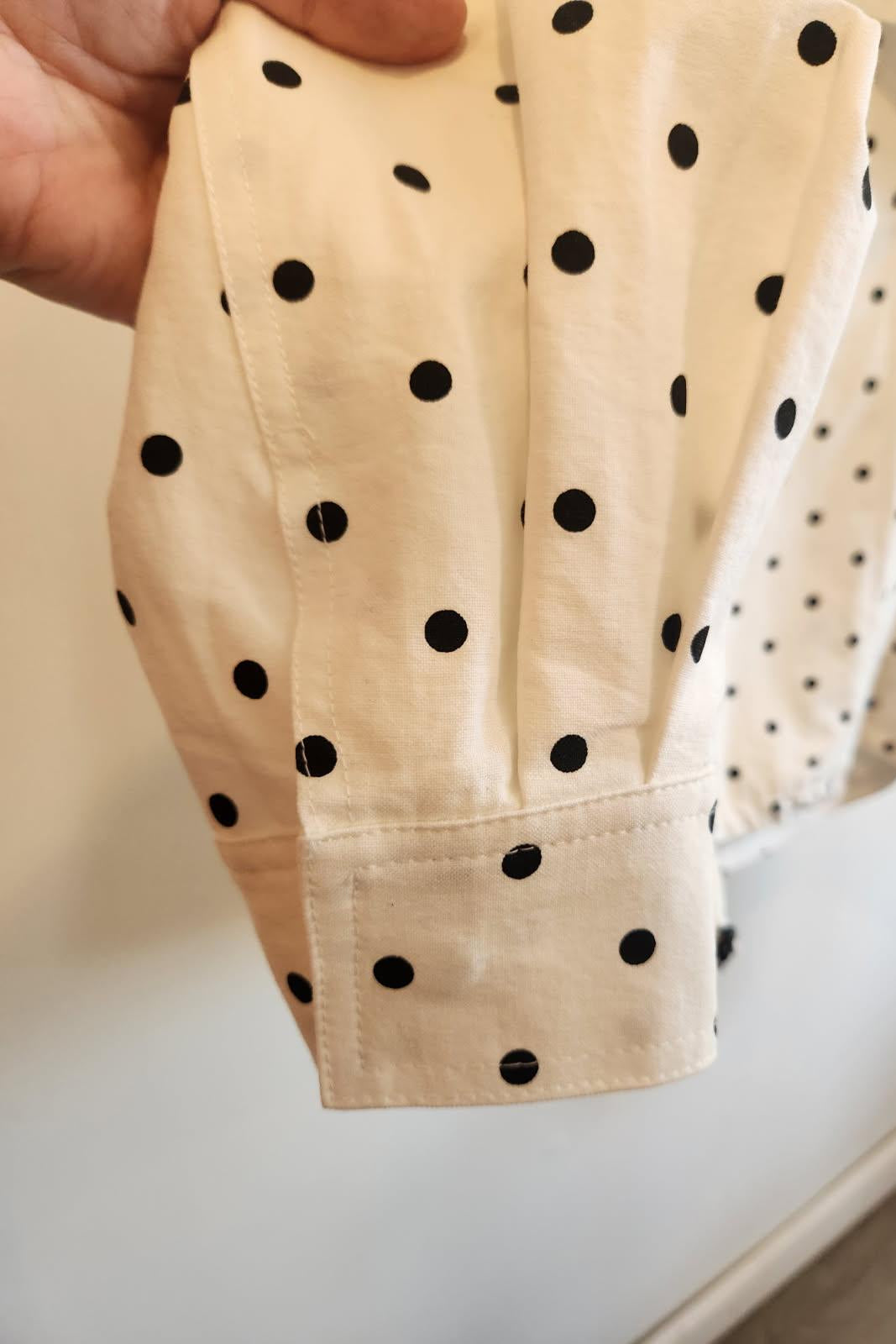 Beige fabric with black polka dots held by a hand on a light background