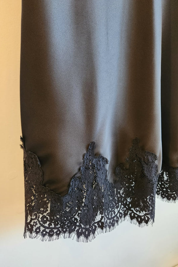 A close-up of a dark gray satin fabric, likely a skirt or dress, featuring a decorative black lace trim along the bottom hem.