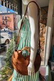 Mannequin wearing a green and white striped dress with a brown leather handbag in a store window.