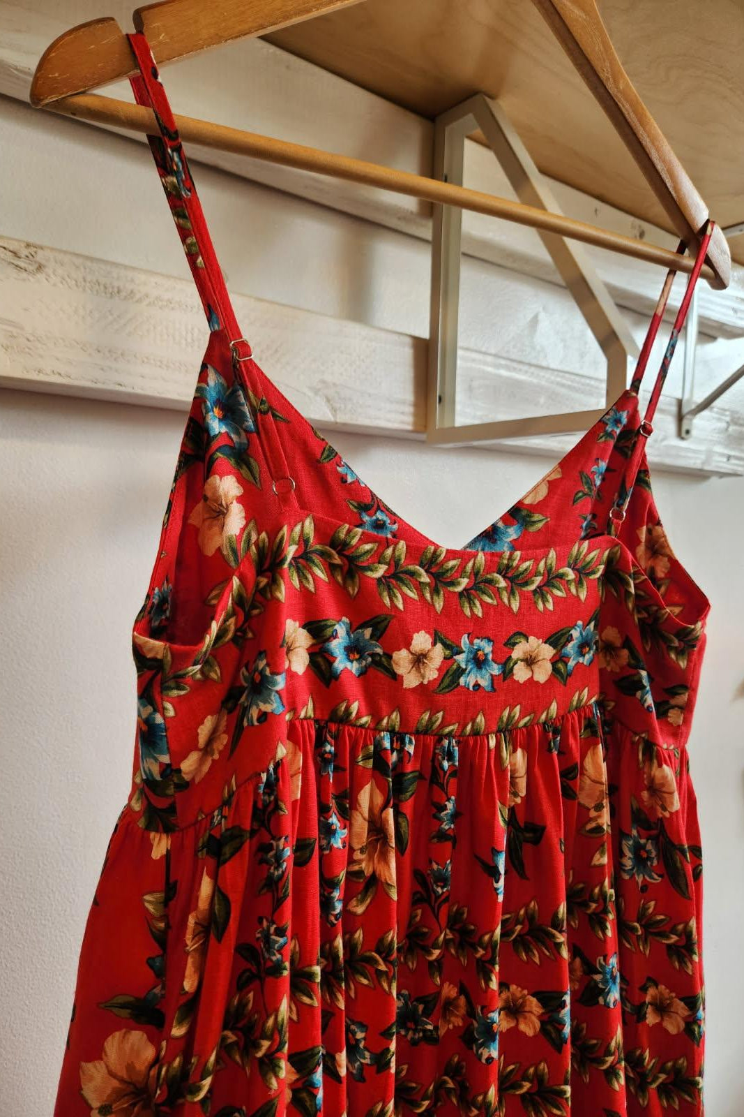 Red floral dress hanging on a wooden hanger against a white wall.