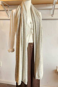 A long, lightweight cream knit scarf draped over a white mannequin torso, styled with a cream cardigan and brown pants in an indoor room setting.