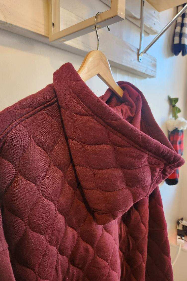 Maroon quilted jacket on a hanger against a neutral background
