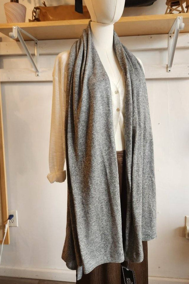 A light gray knit wrap or shawl draped over a cream-colored button-front cardigan and brown pants, displayed on a headless mannequin in a boutique setting.