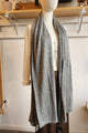 A light gray knit wrap or shawl draped over a cream-colored button-front cardigan and brown pants, displayed on a headless mannequin in a boutique setting.