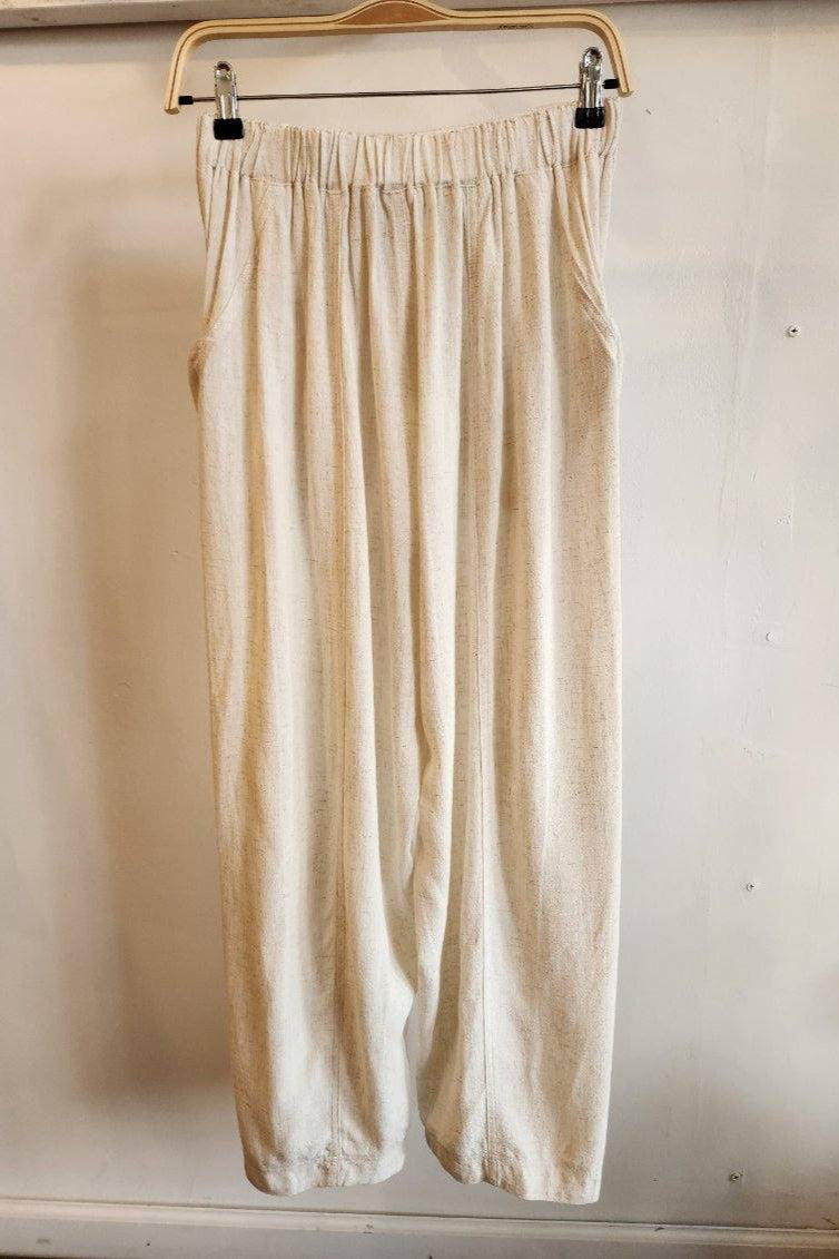 Beige pants hanging on a wooden hanger against a white wall.