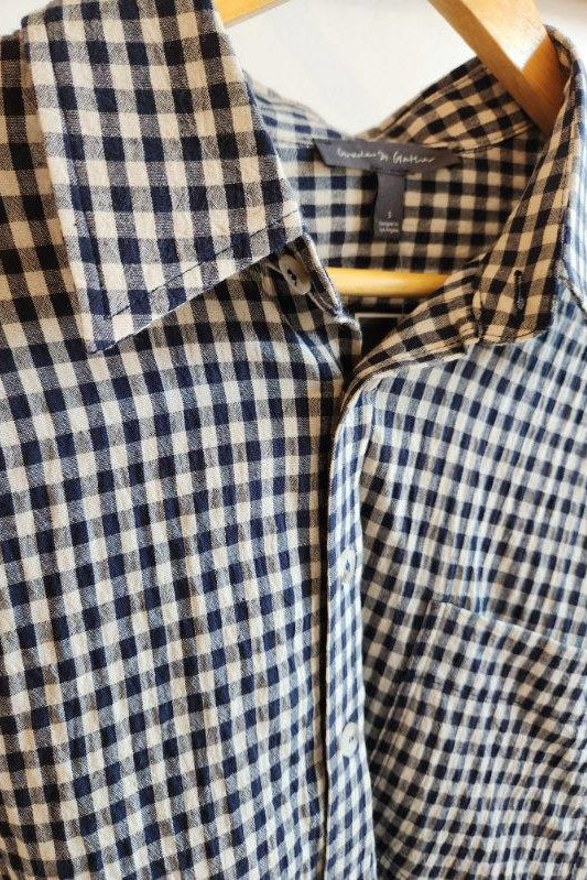 A close-up of a navy and beige gingham checkered button-down shirt hanging on a wooden hanger. The brand label inside the collar reads 'society6 fashion'.