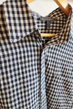 A close-up of a navy and beige gingham checkered button-down shirt hanging on a wooden hanger. The brand label inside the collar reads 'society6 fashion'.