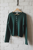 Green cardigan on a wooden hanger against a white brick wall