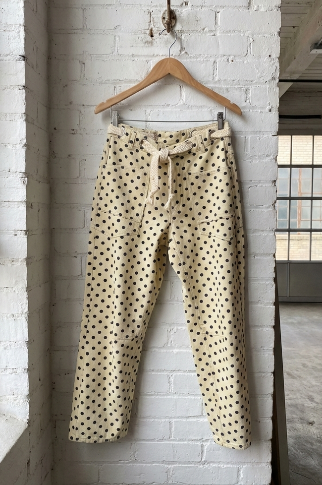 Polka dot pants hanging on a wooden hanger against a white brick wall.