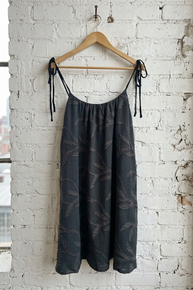 Dark patterned dress hanging on a wooden hanger against a white brick wall.
