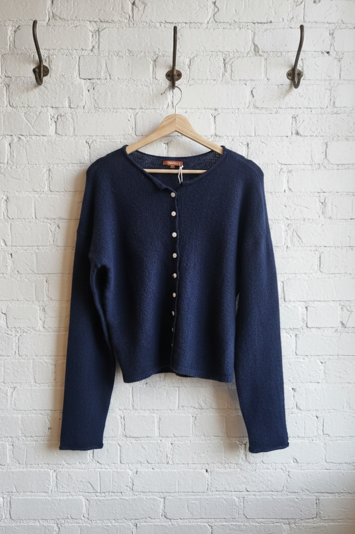 Navy blue cardigan hanging on a wooden hanger against a white brick wall.