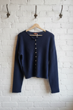 Navy blue cardigan hanging on a wooden hanger against a white brick wall.
