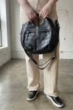 Person holding a black leather bag in an indoor setting with a white brick wall.
