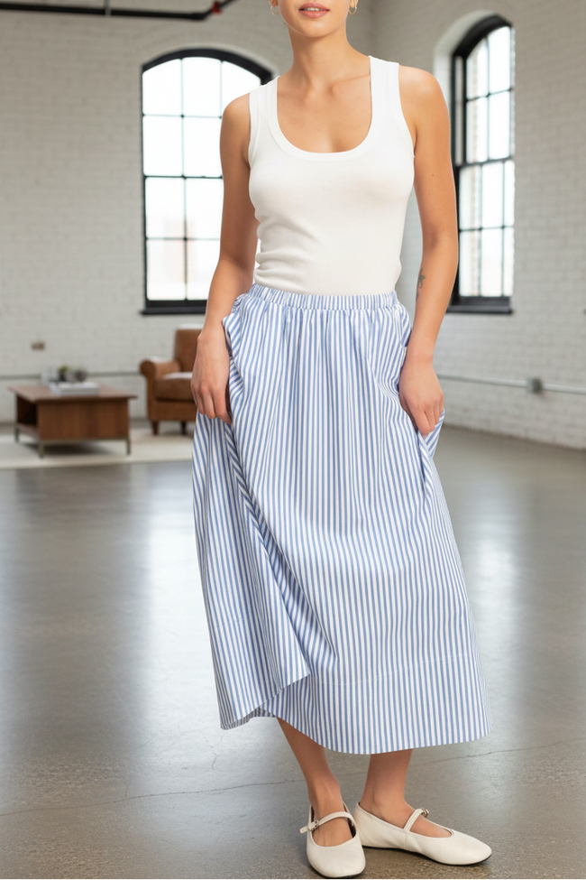 Woman wearing a white tank top and blue striped skirt in a large room with high ceilings and large windows.