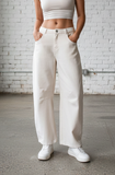 Woman wearing a white crop top and pants standing in a room with white brick walls.