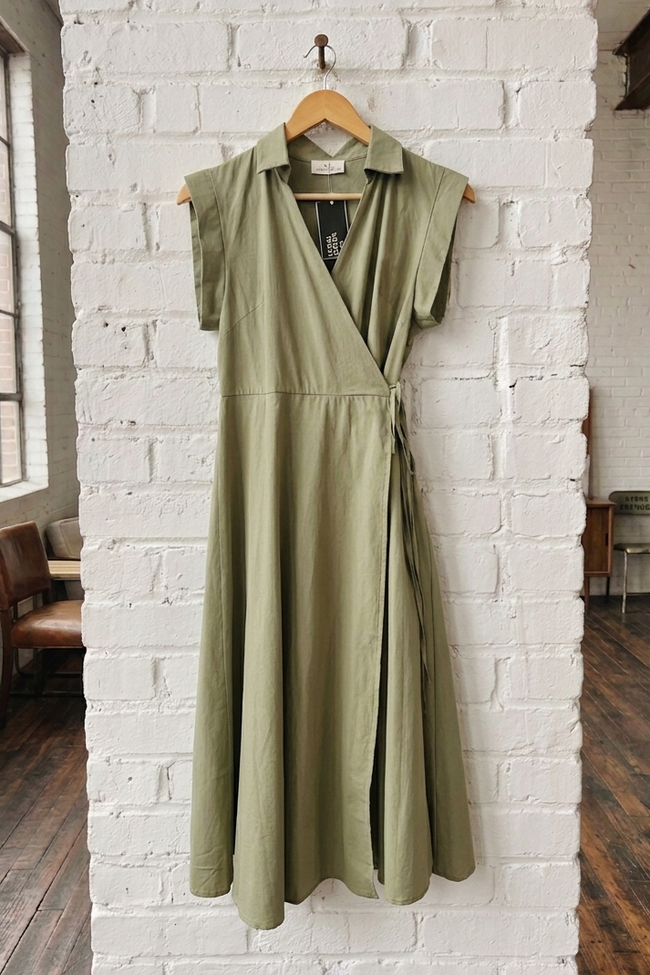 Green dress hanging on a wooden hanger against a white brick wall.