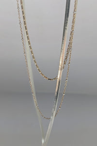 Three layered gold-tone and silver chain necklaces displayed on a neutral gray background.