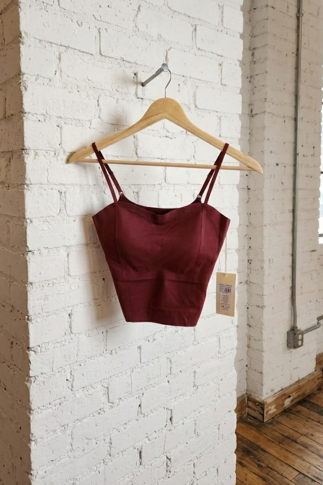 Maroon crop top on a wooden hanger against a white brick wall.