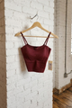 Maroon crop top on a wooden hanger against a white brick wall.