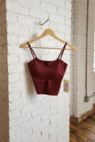 Maroon crop top on a wooden hanger against a white brick wall.
