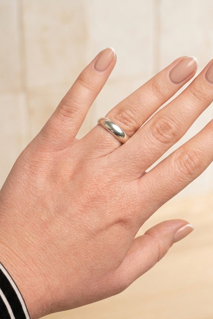 Hand wearing a silver ring on a beige background