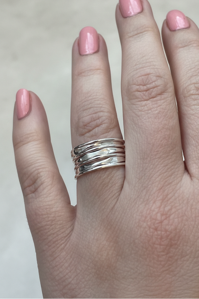 Hand with pink nail polish wearing a silver ring on a neutral background